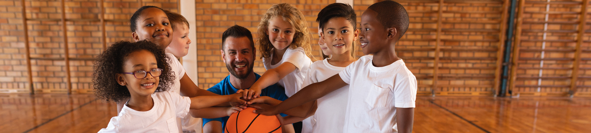 Jovens e treinador com as mãos à volta de uma bola de basquetebol